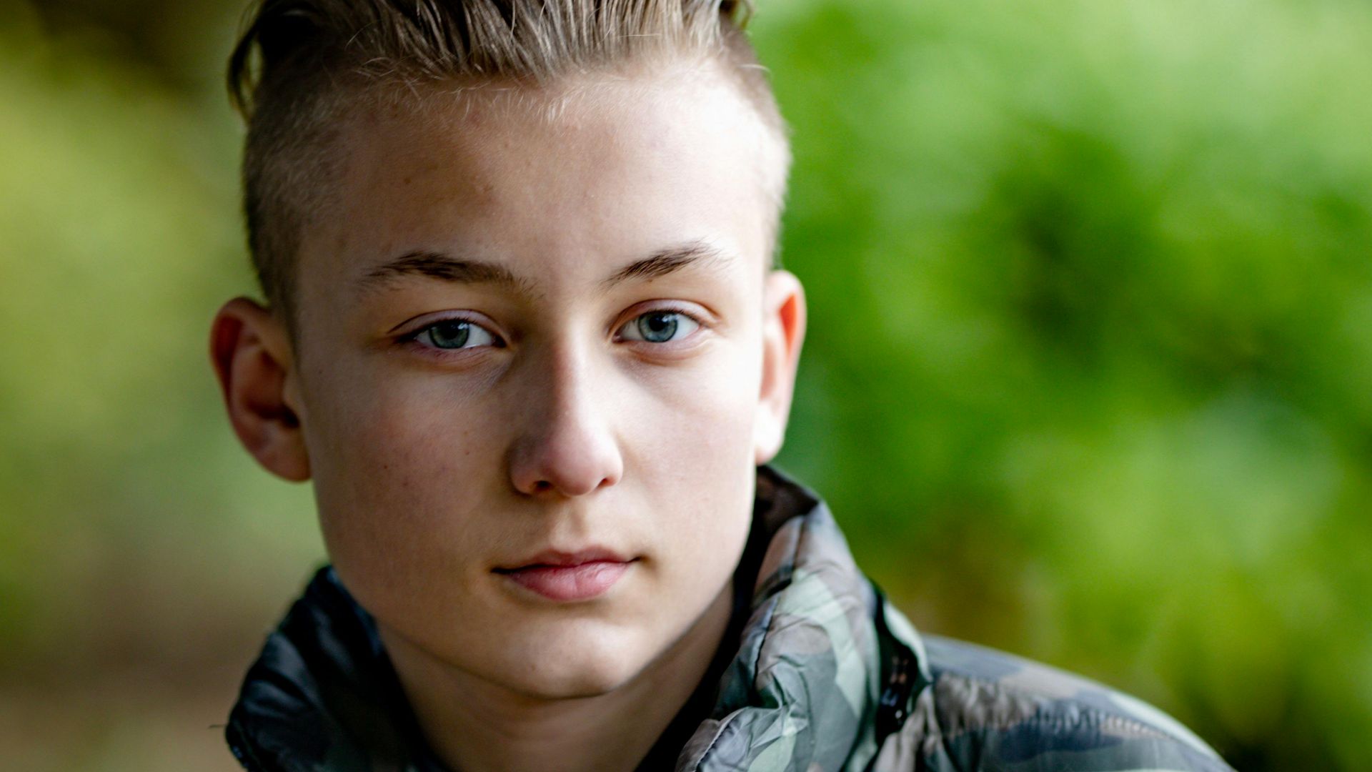 Portrait of a teenage boy wearing a camouflage jacket outdoors in natural light.