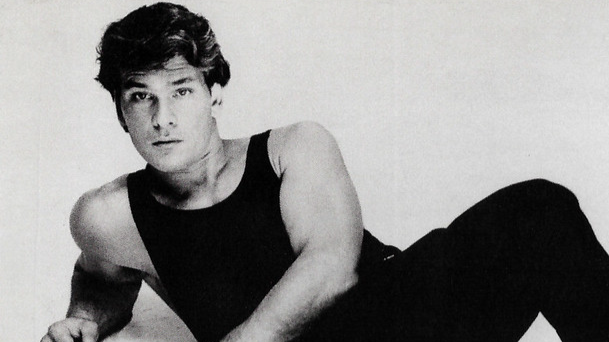 Grayscale photo of actor Patrick Swayze wearing a black outfit and lying on the floor