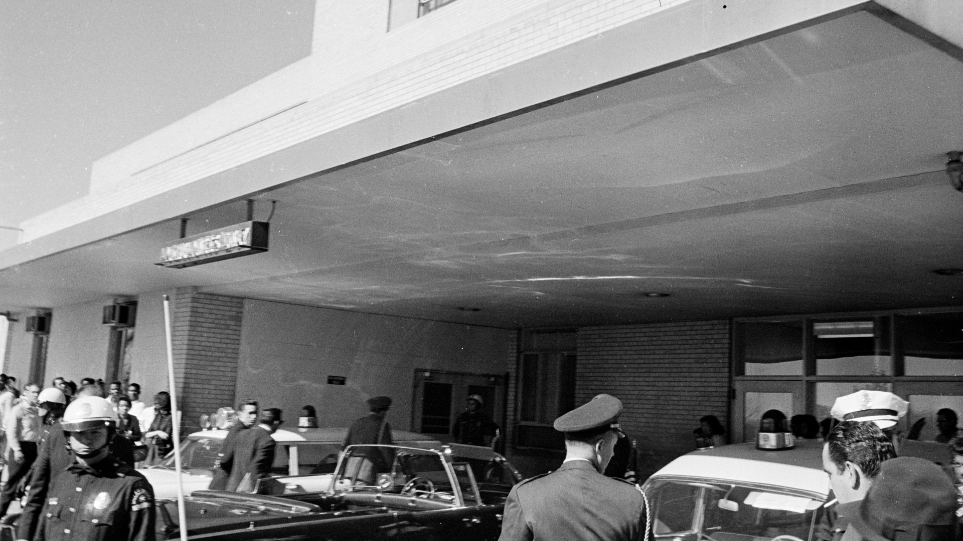Police officers and bystanders gather in front of an entrance to Parkland Hospital in Dallas, Texas, following the arrival of the Presidential limousine carrying President John F. Kennedy.