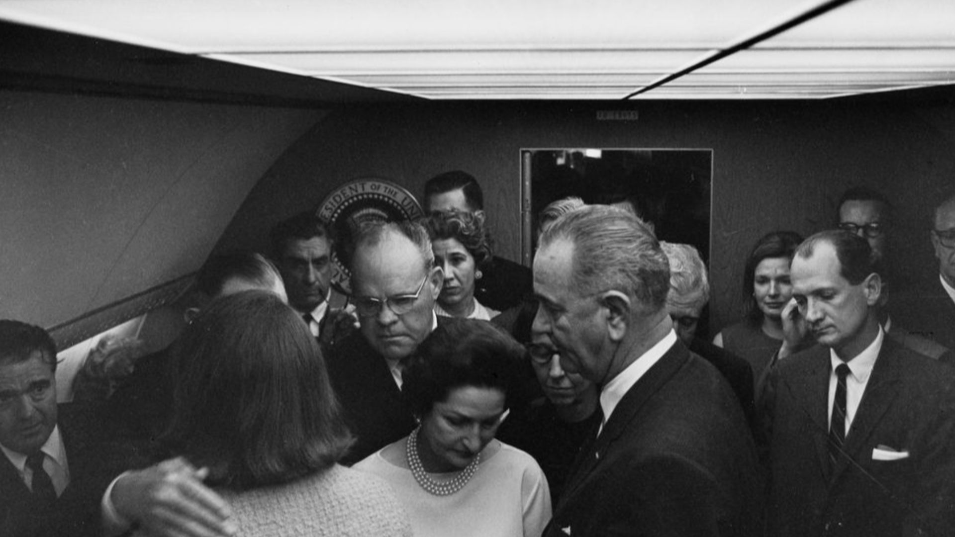 Officials gather inside Air Force One for the swearing-in of President Lyndon B. Johnson at Love Field in Dallas, Texas, following the assassination of President John F. Kennedy. Left to right: media liaison, Jack Valenti; former first lady, Jacqueline Kennedy (back to camera); Representative Albert Thomas of Texas (mostly hidden); dean of the White House press corps and United Press International (UPI) reporter, Merriman