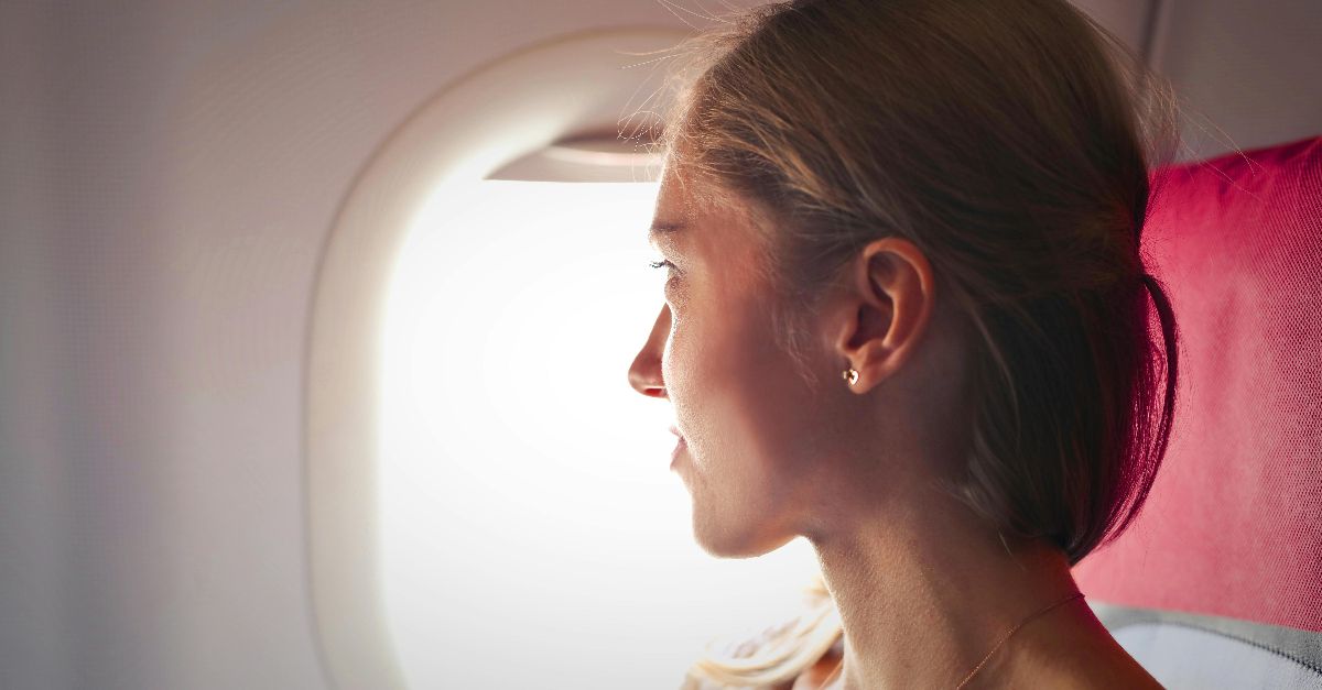 A woman gazes thoughtfully out the window of an airplane during her journey.