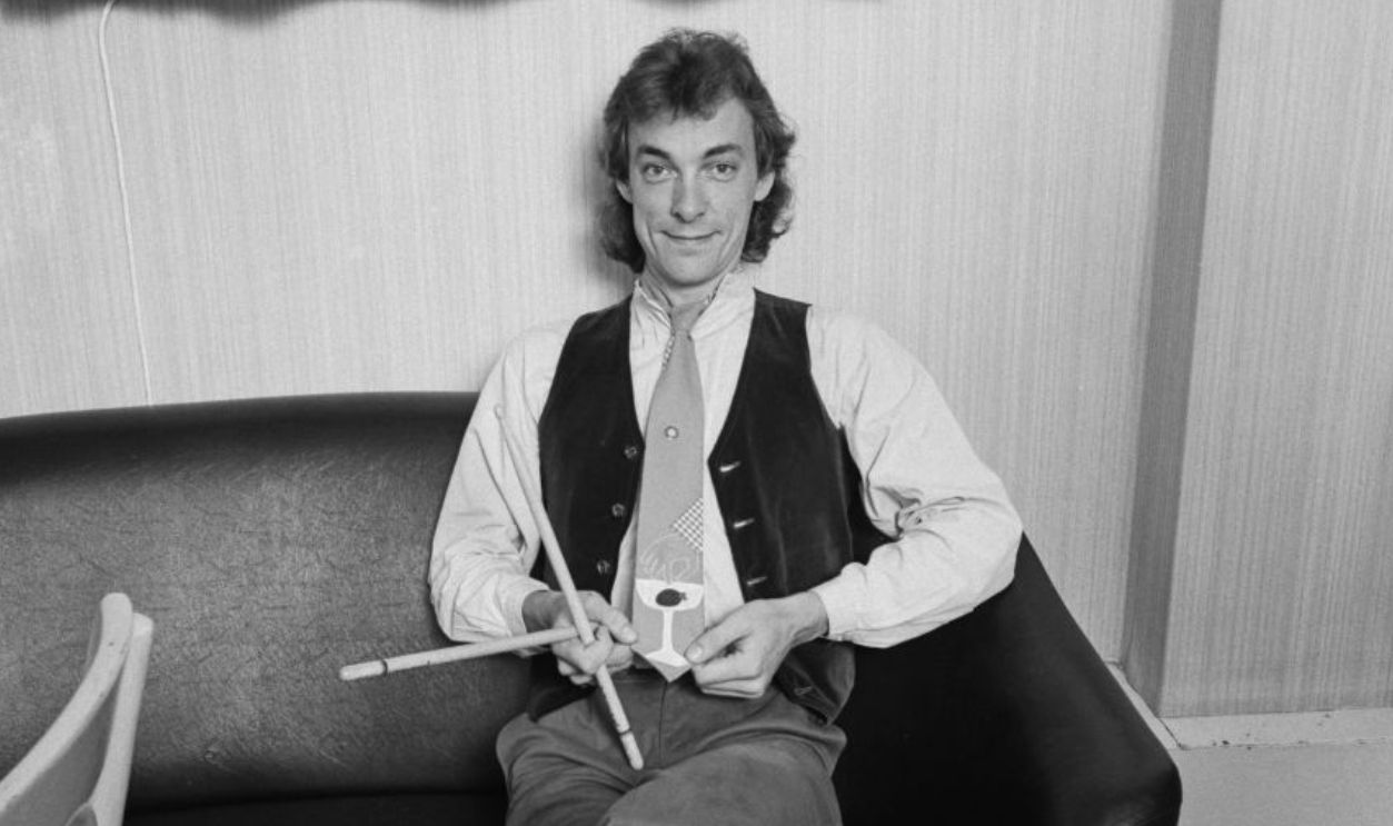 Drummer and lyricist Neil Peart (1952 - 2020) of Canadian progressive rock group, Rush, showing off a novelty tie, backstage, 1980.