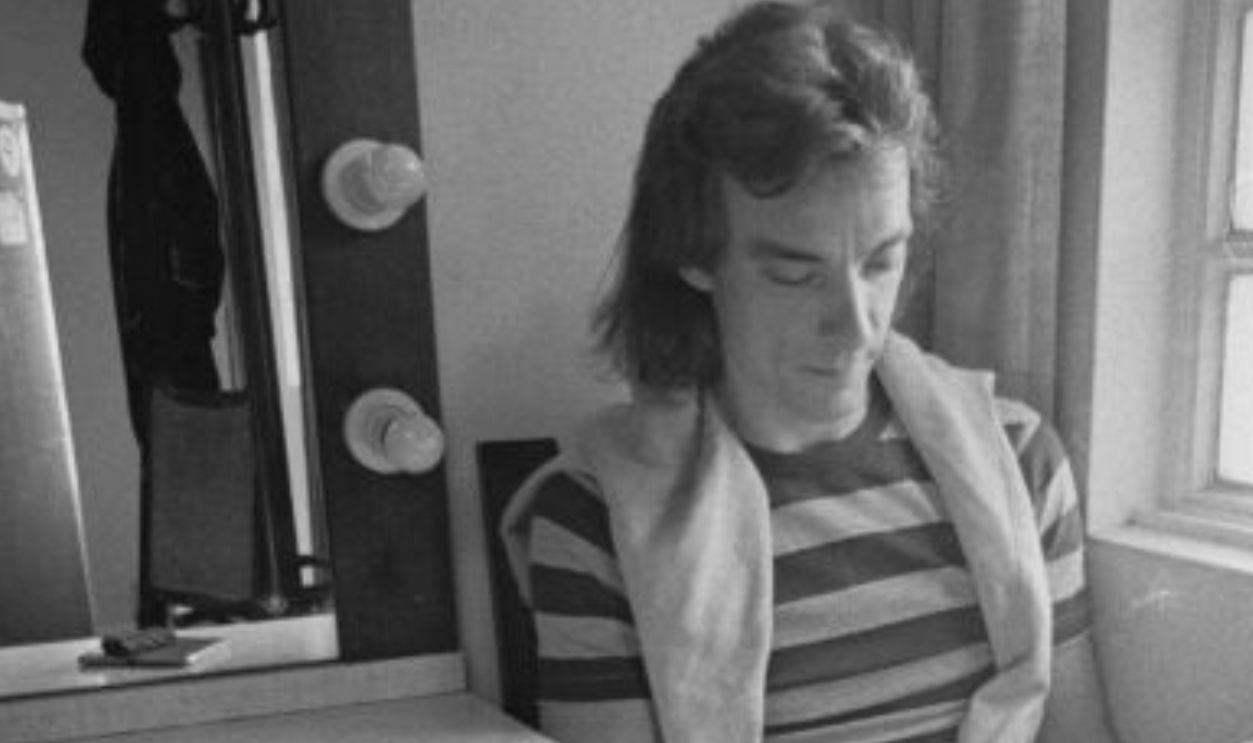 Drummer and lyricist Neil Peart (1952 - 2020) of Canadian progressive rock group, Rush, reading a book in his dressing room, 1980.