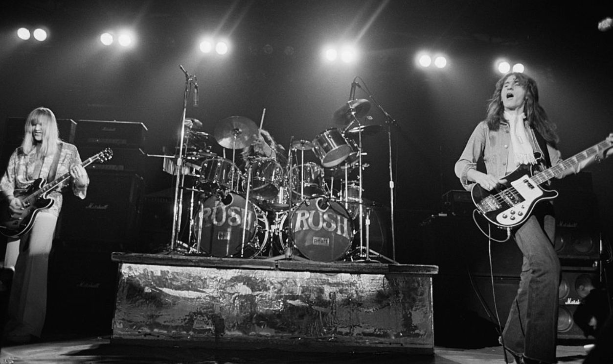 Canadian progressive rock group, Rush, performing at the Civic Center in Springfield, Massachusetts, during their All The World's a Stage tour, 9th December 1976. Left to right: Alex Lifeson, Neil Peart (behind drum kit) and Geddy Lee. 