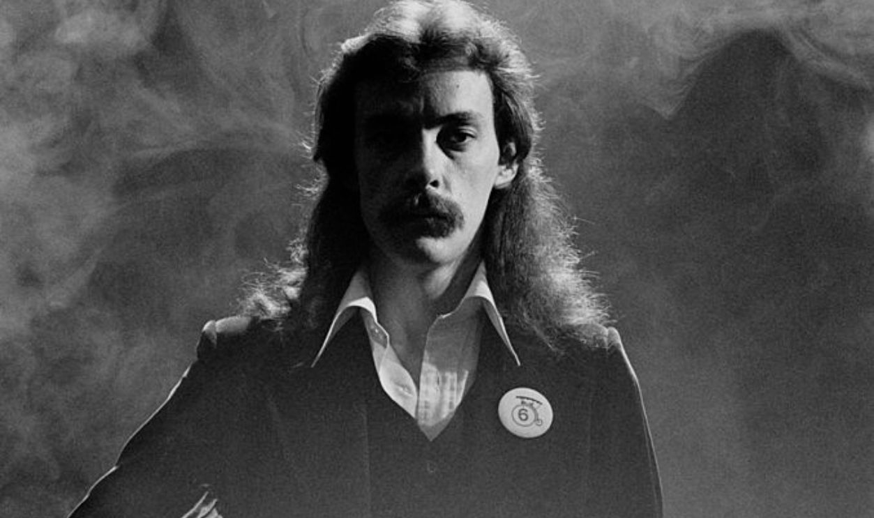 Neil Peart, drummer with Canadian rock band Rush, poses with one hand on his hip, with a smoke behind him in a studio portrait, 1978. 