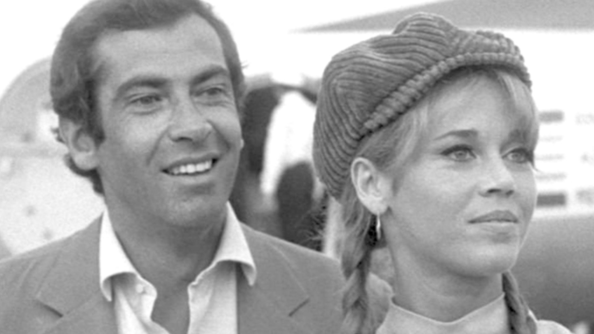 Sur le tarmac d'un aéroport, Roger Vadim est placé derrière Jane Fonda. Il sourit en regardant vers sa gauche et elle semble sereine en regardant dans la même direction, avec un très léger sourire. Il porte les cheveux bruns, épais. Il est vêtu d'une veste gris clair et d'une chemise blanche au col ouvert. Elle porte une casquette et les cheveux longs chatain clair, avec deux nattes.  Elle est vêtue d'une robe gris clair aux bras nus avec col Mao.