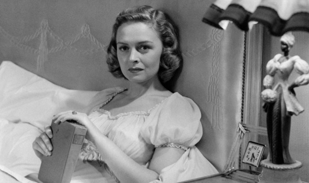 American actress Donna Reed (Donnabelle Mullenger) lying in a bed holding a book in the film Beyond Glory. 1948