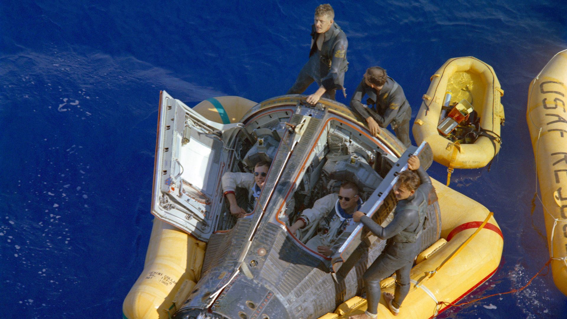Astronauts Neil A. Armstrong (right) and David R. Scott (left) sit with their spacecraft hatches open while awaiting the arrival of the recovery ship, the USS Leonard F. Mason after the successful completion of their Gemini VIII mission. They are assisted by U.S. Air Force Pararescuemen, who jumped to their spacecraft.  The Pararescuemen are:  A/2C Glenn M. Moore (by the hatch), A/1C Eldridge M. Neal (upper left); and S/Sgt Larry D. Huyett (center standing on the floatation collar).  
The overhead view shows the Gemini 8 spacecraft with the yellow flotation collar attached to stabilize the spacecraft in choppy seas. The green marker dye is highly visible from the air and is used as a locating aid.