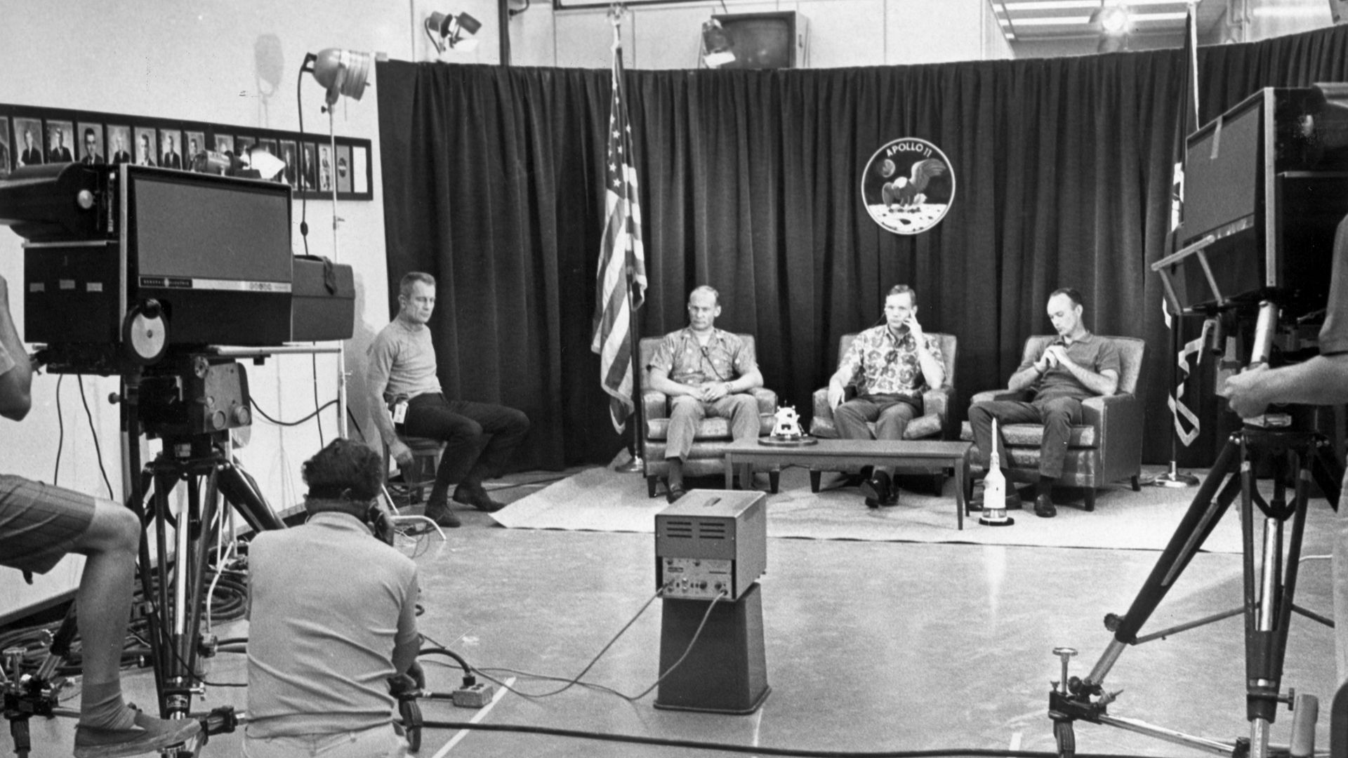 Deke Slayton (on stool at left), Buzz Aldrin, Neil Armstrong, and Michael Collins during the last pre-flight press conference. At far left is chief astronaut and director of flight crew operations, Donald K. Slayton. The press conference with questions via intercom, was held under semi-isolation conditions to avoid exposing the astronauts to possible illness at the last minute.