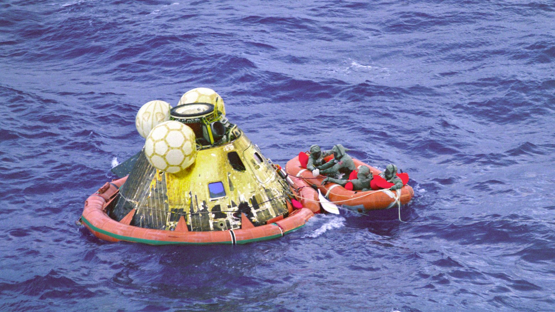 The Apollo 11 crew await pickup by a helicopter from the USS Hornet, prime recovery ship for the historic Apollo 11 lunar landing mission. The fourth man in the life raft is a United States Navy underwater demolition team swimmer. All four men are wearing Biological Isolation Garments (BIG). The Apollo 11 Command Module