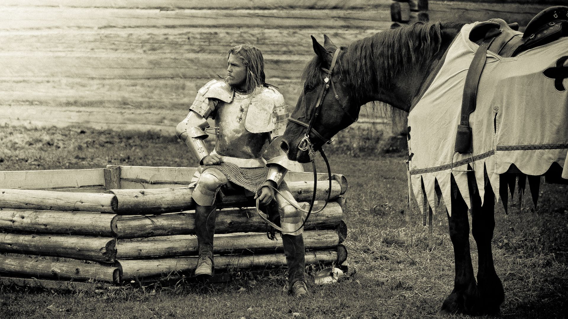 Artistic, black-and-white photographic rendition of an armored knight pensively looking off to the side. They are accompanied by their horse.