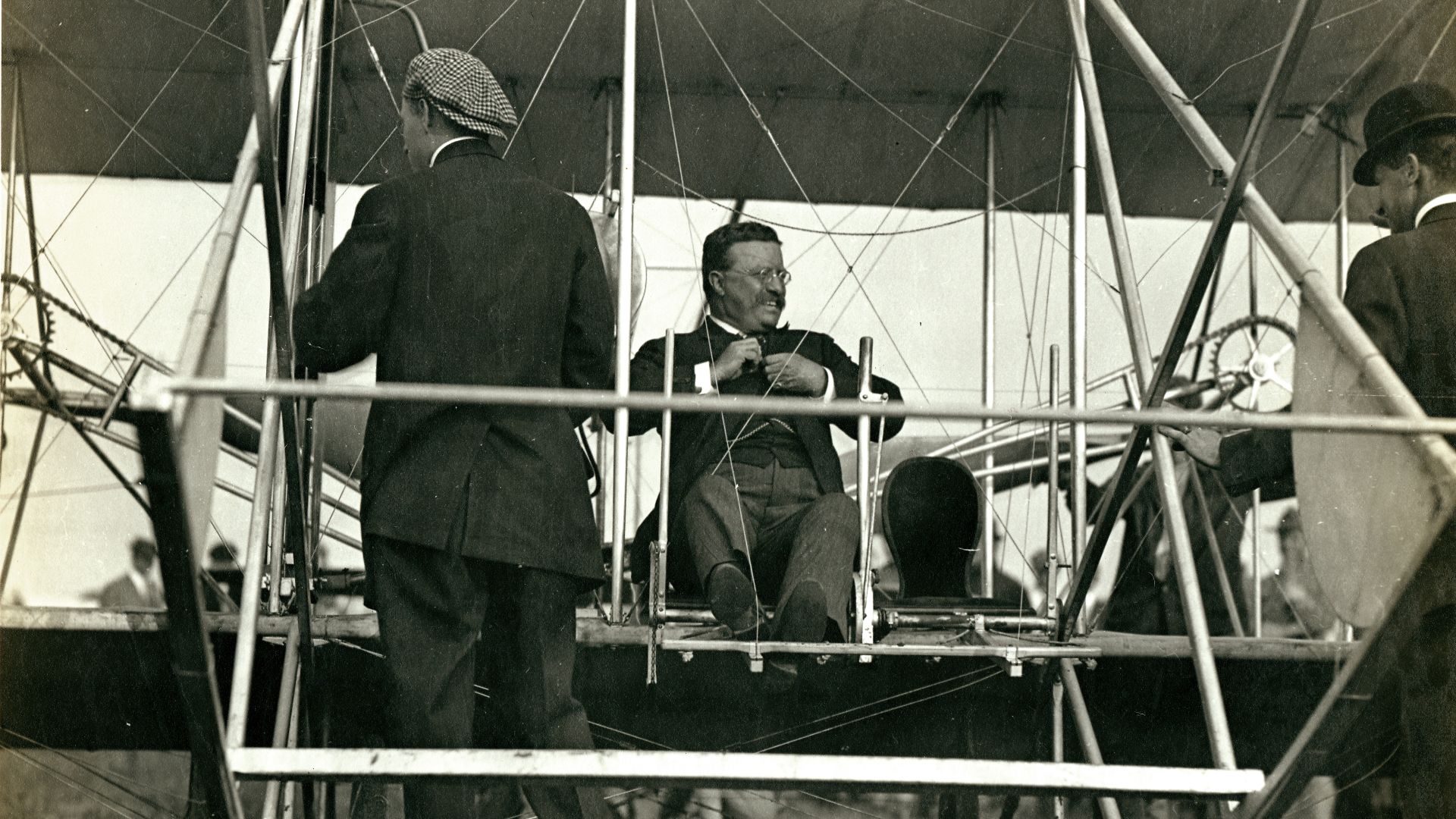 Title: President Theodore Roosevelt prepares to take his first airplane ride with pilot Arch Hoxsey (back to camera) at Kinloch Field during the 1910 International Aeronautic Tournament.