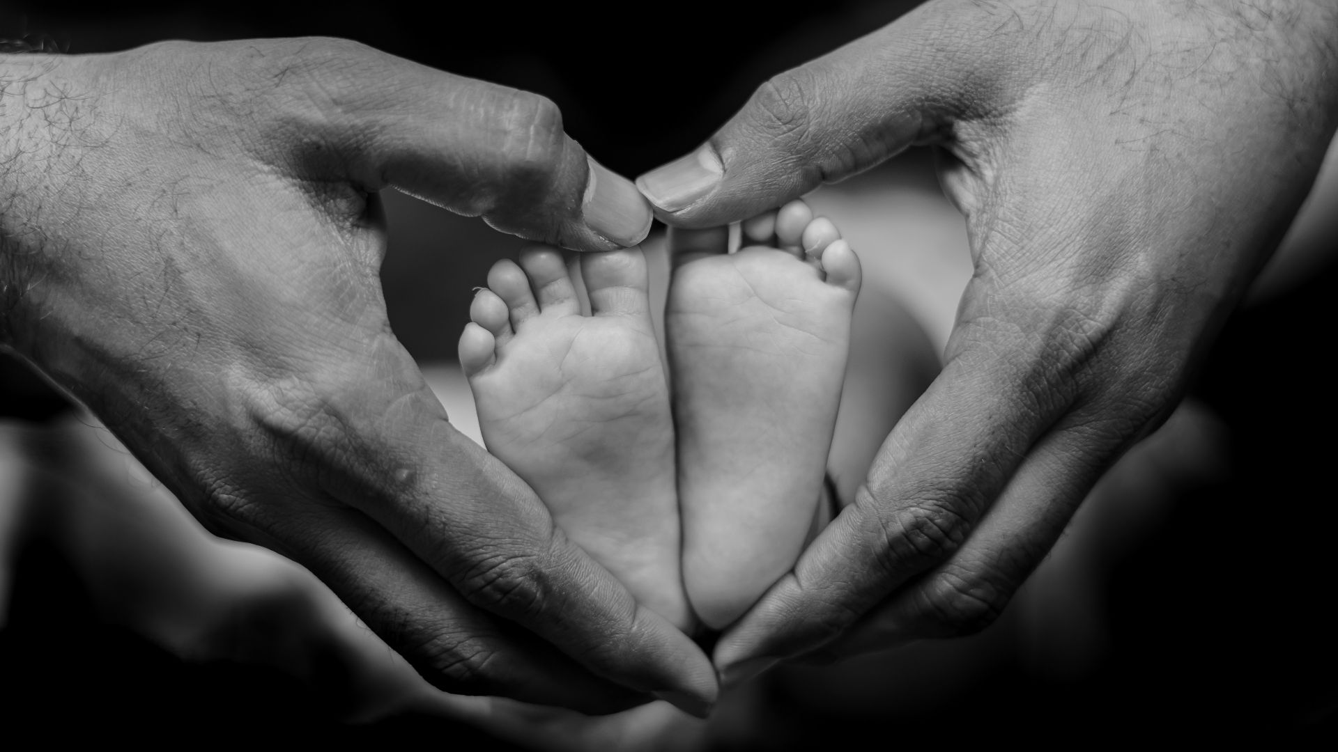 a black and white photo of two hands holding a baby's feet
