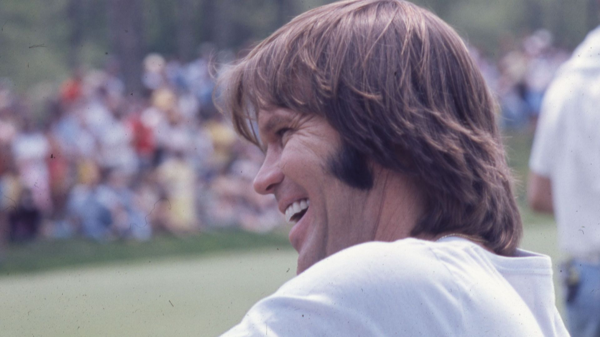 A view of musician Glen Campbell during the 1977 Memorial Tournament pro-am at the Muirfield Village Golf Club. Crowds of spectators are in the distance. Campbell played in a sixsome that also included former United State President Gerald Ford, professional golfers Jack Nicklaus and Roger Maltbie, and actor and comedians Jackie Gleason and Bob Hope.