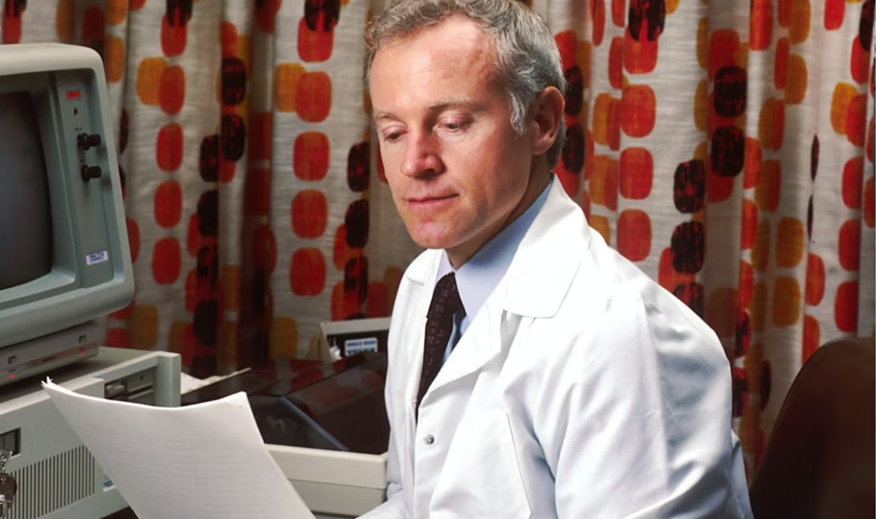 man reading papers in front of computer