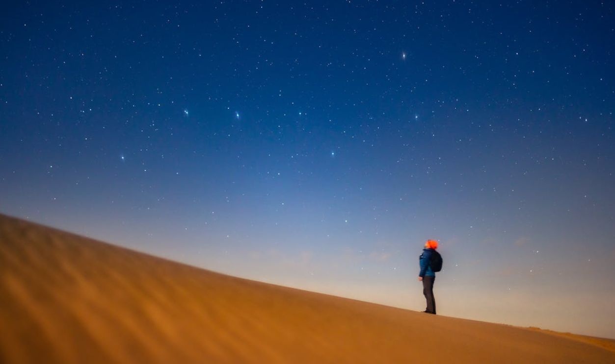 A person standing on top of a sand dune looking up at the stars