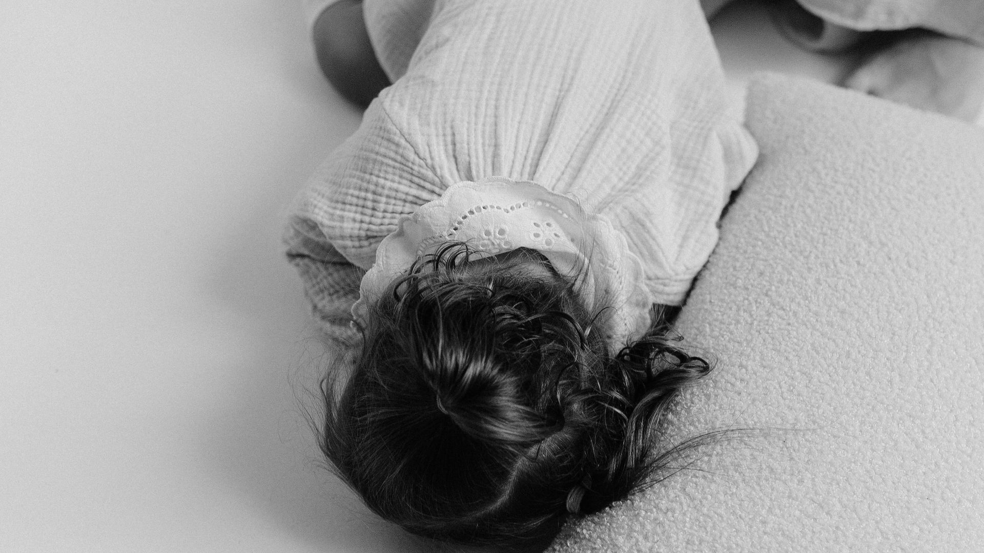 Black and white photo of a child peacefully sleeping indoors on a soft pillow.