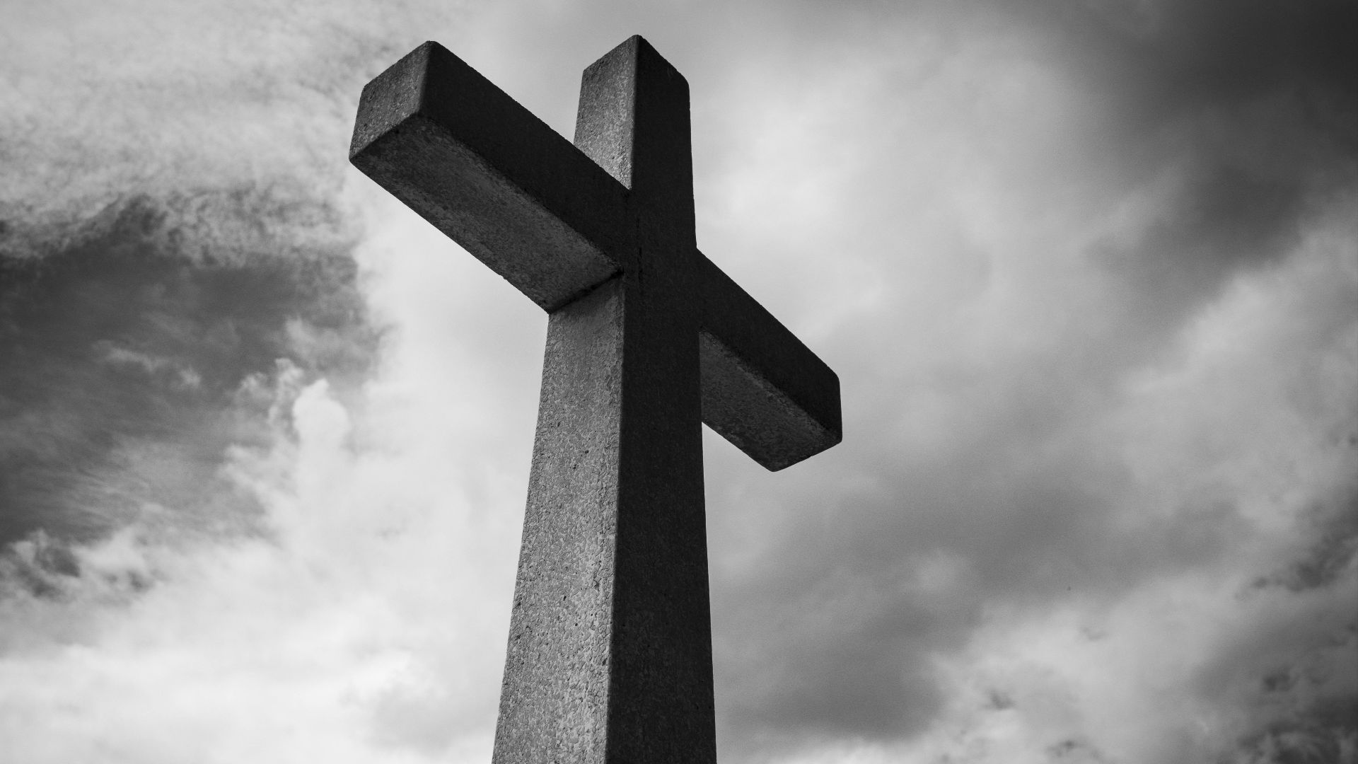 A black and white photo of a cross set against a dramatic, cloudy sky, symbolizing spirituality and faith.