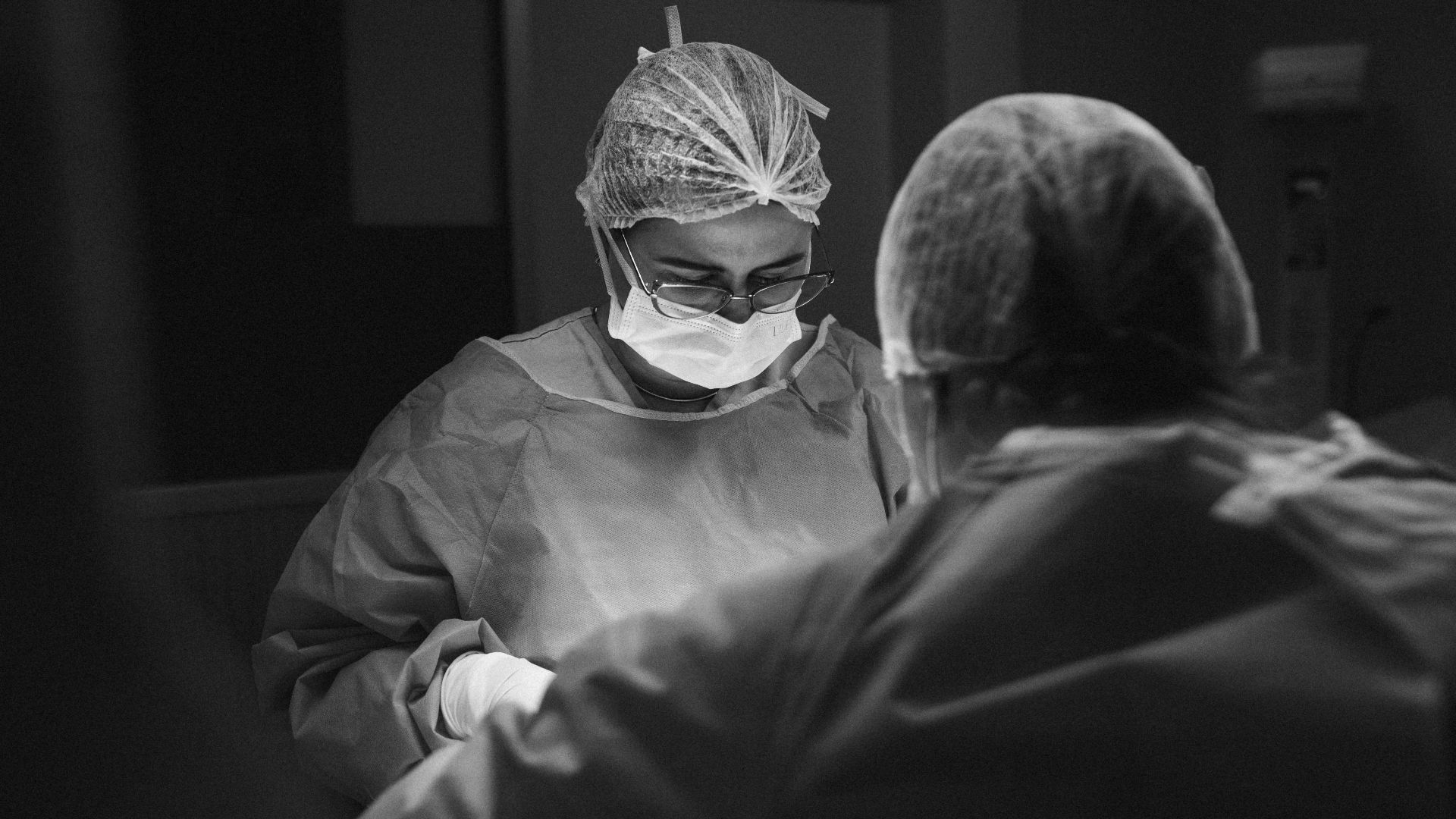 Two surgeons operate under focused lighting in a sterile environment.