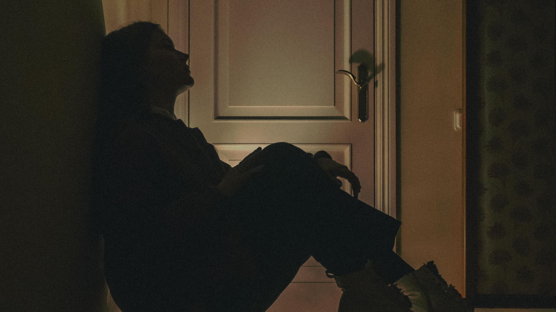 A silhouette of a woman sitting against a wall in a dimly lit room, conveying solitude and introspection.