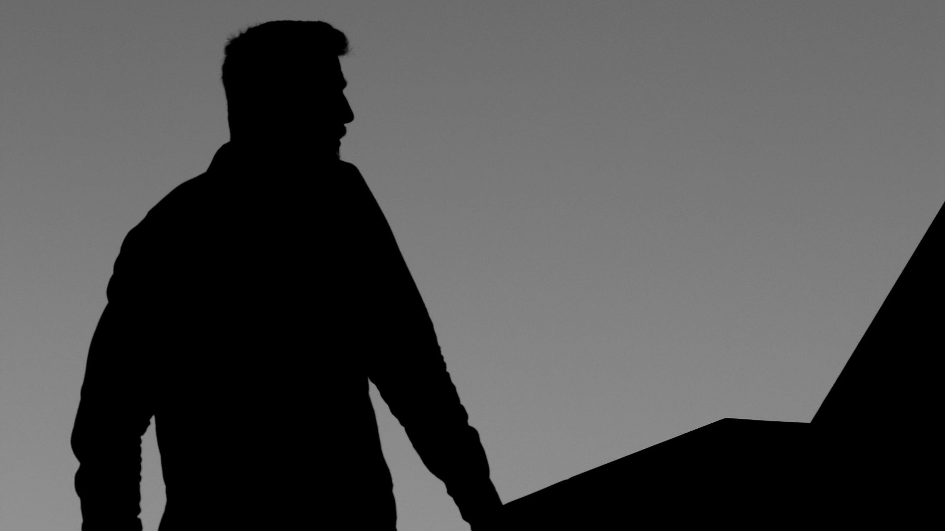 A silhouette of a young man standing dramatically against the sky at dawn.