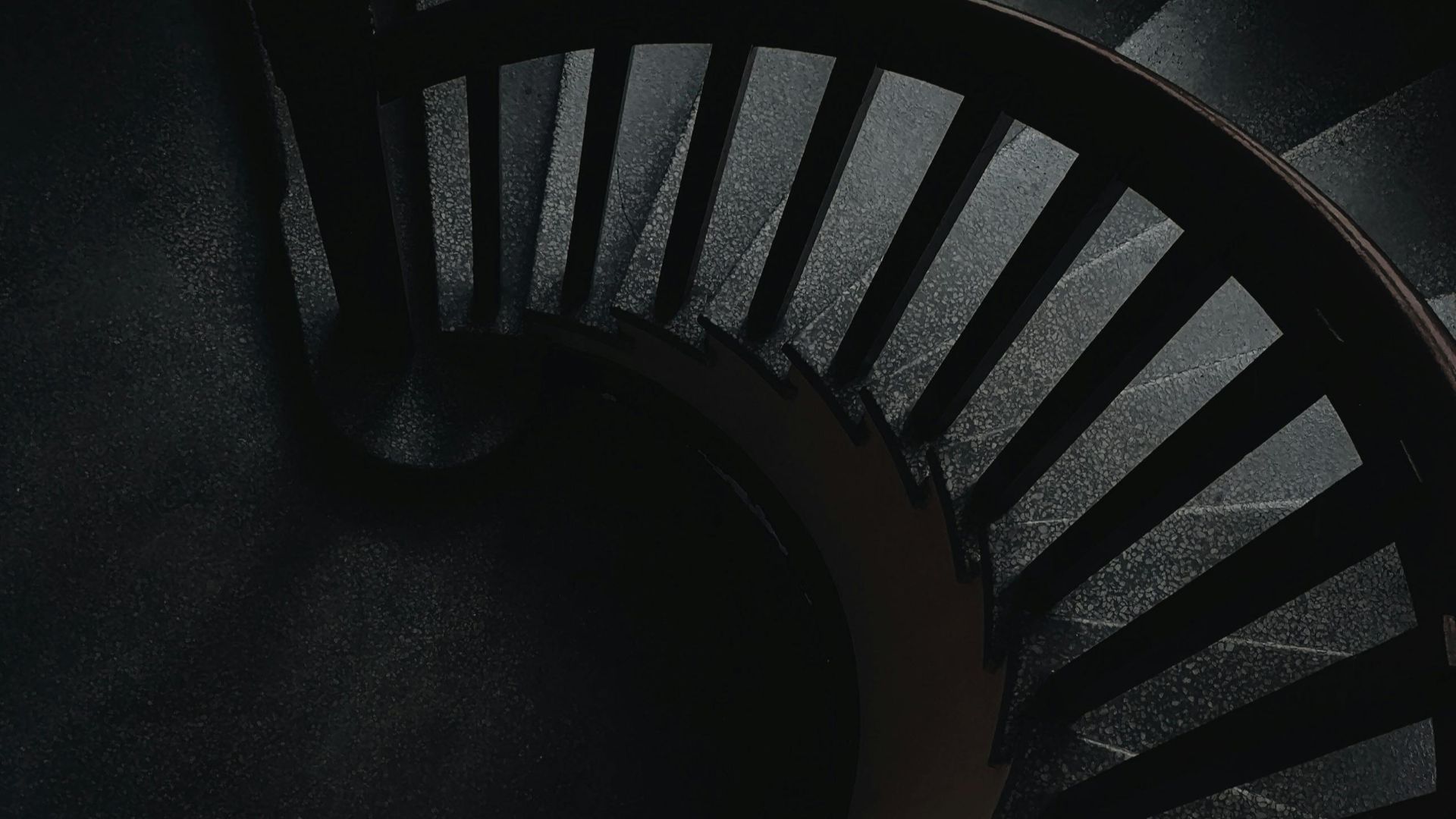 A dark, architectural spiral staircase featuring modern geometry in a monochrome setting.
