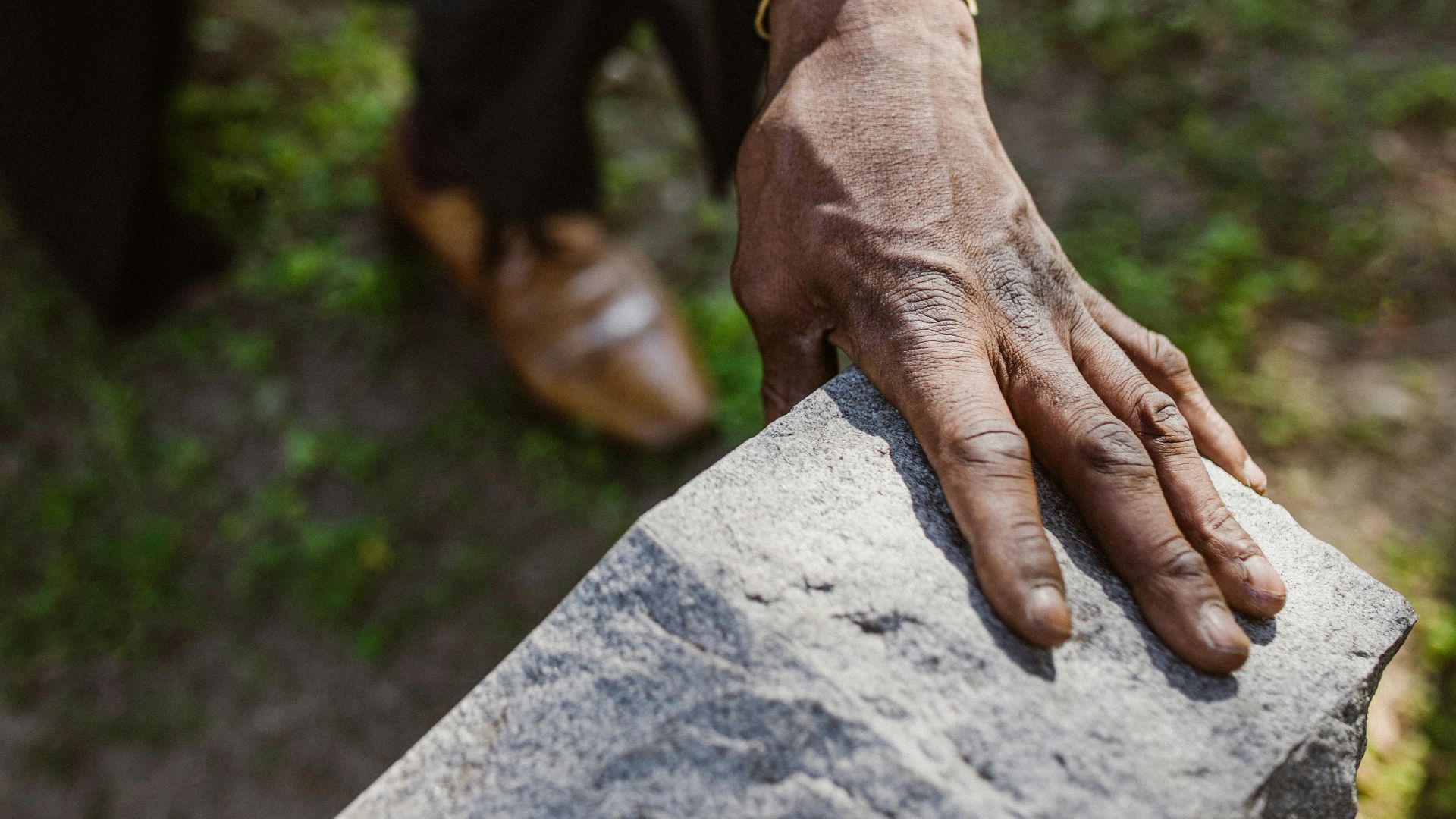 A man mourns a loved one, holding a rose by a gravestone, signifying loss and remembrance.