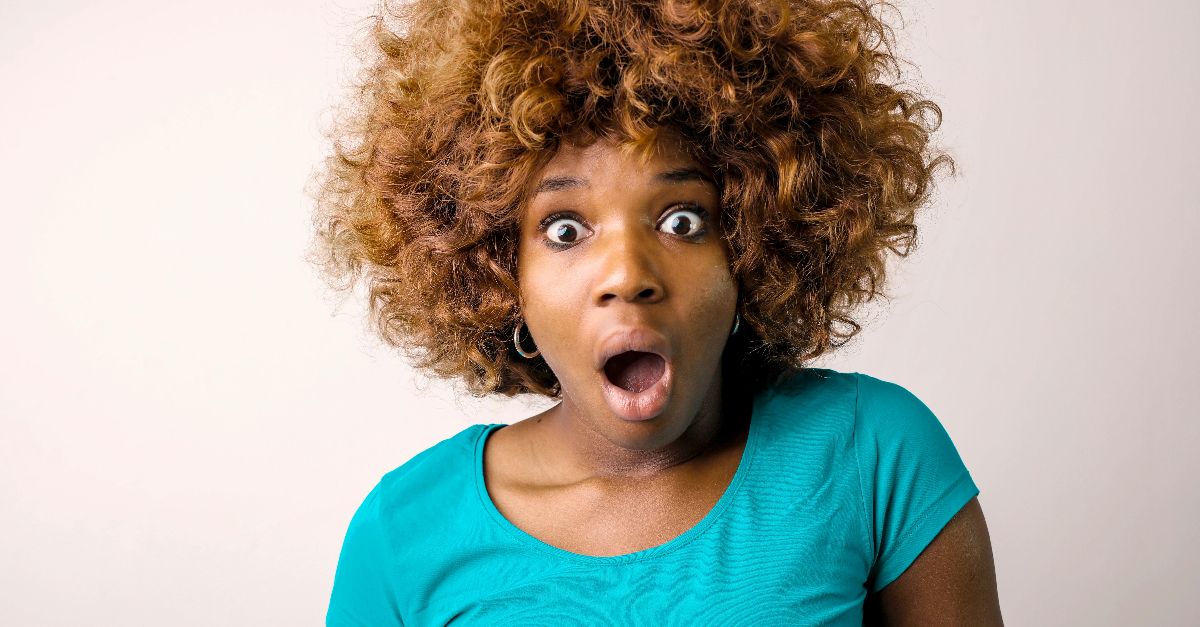 Portrait of a surprised woman with curly hair in a teal top on a white background.