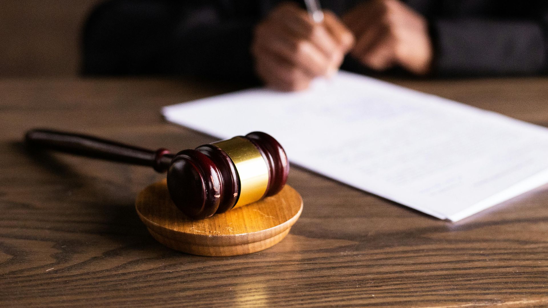 Judge signing documents at desk with focus on gavel, representing law and justice.