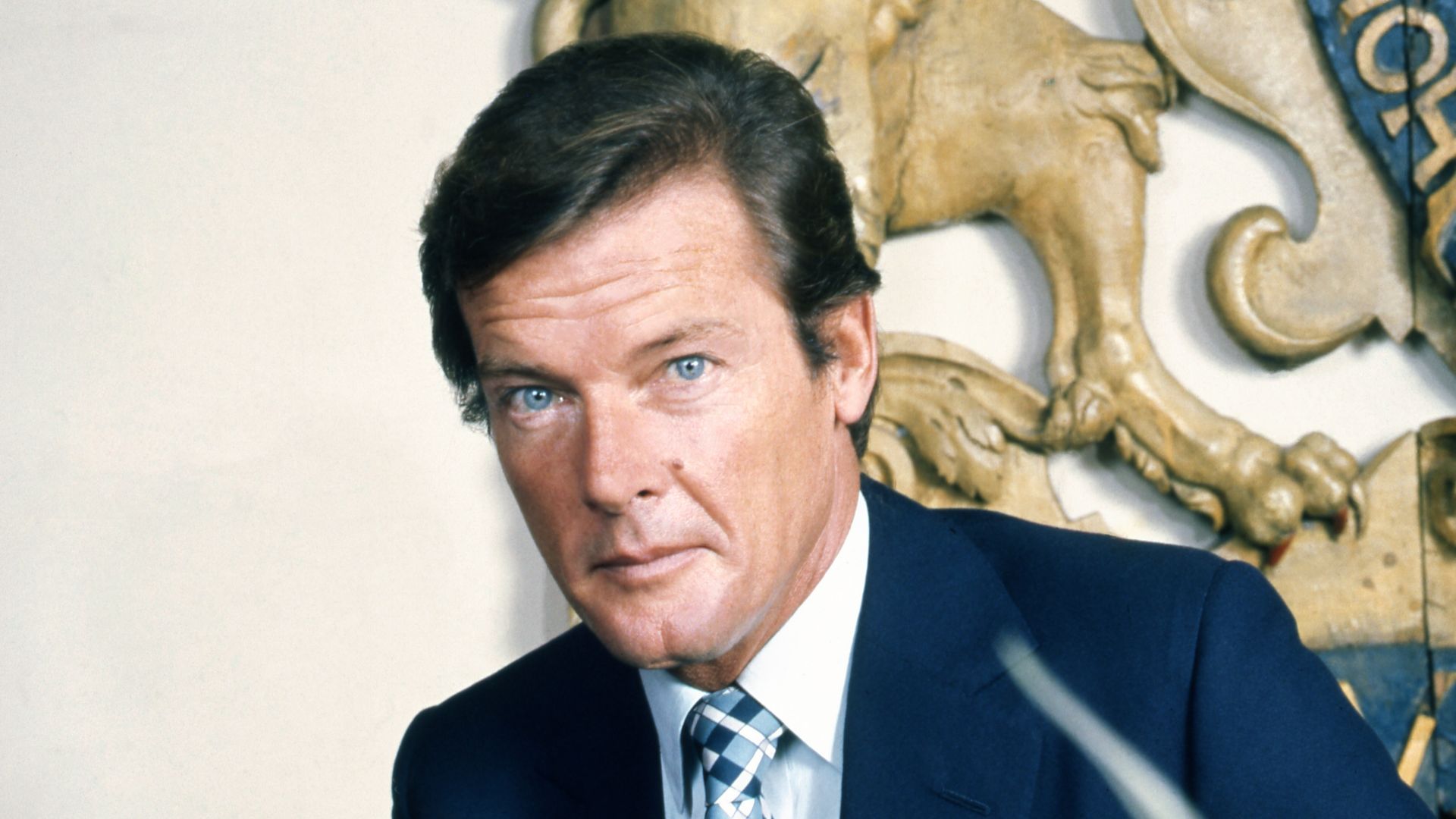 Portrait of Sir Roger Moore sitting on the photographer's bed.