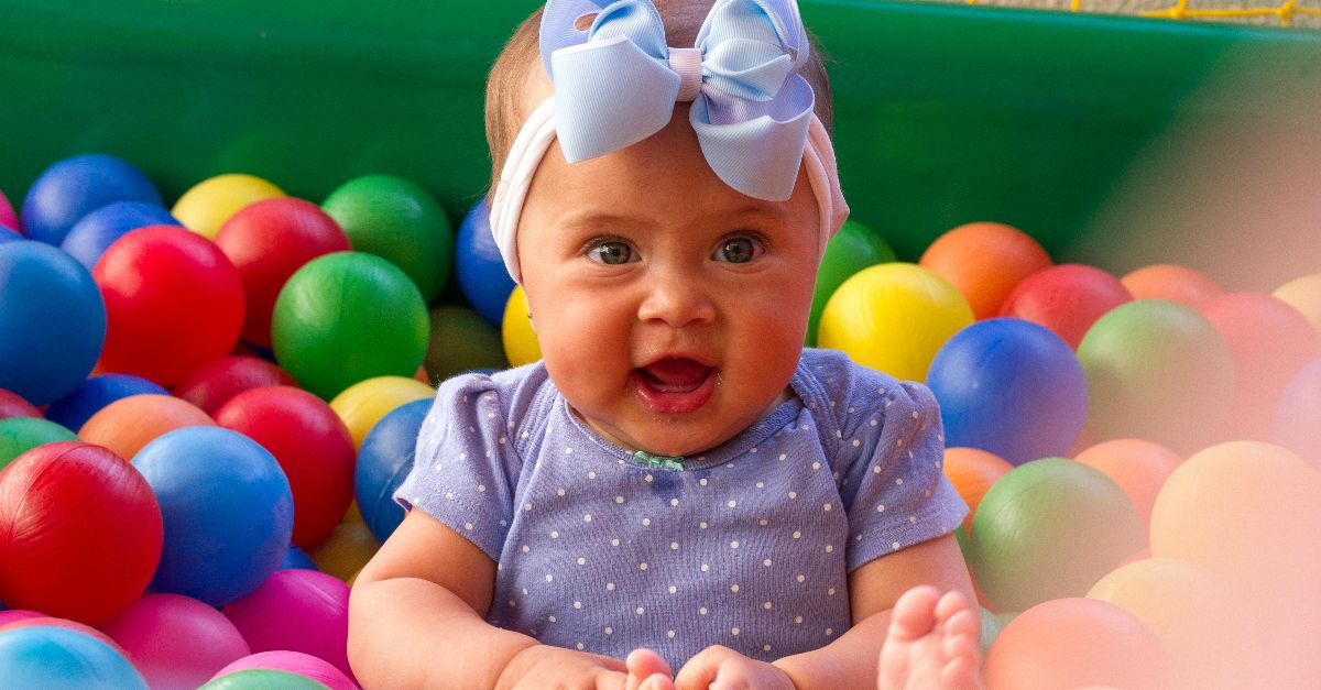 Charming baby with blue bow smiling amidst vibrant plastic balls. Perfect for childhood themes.