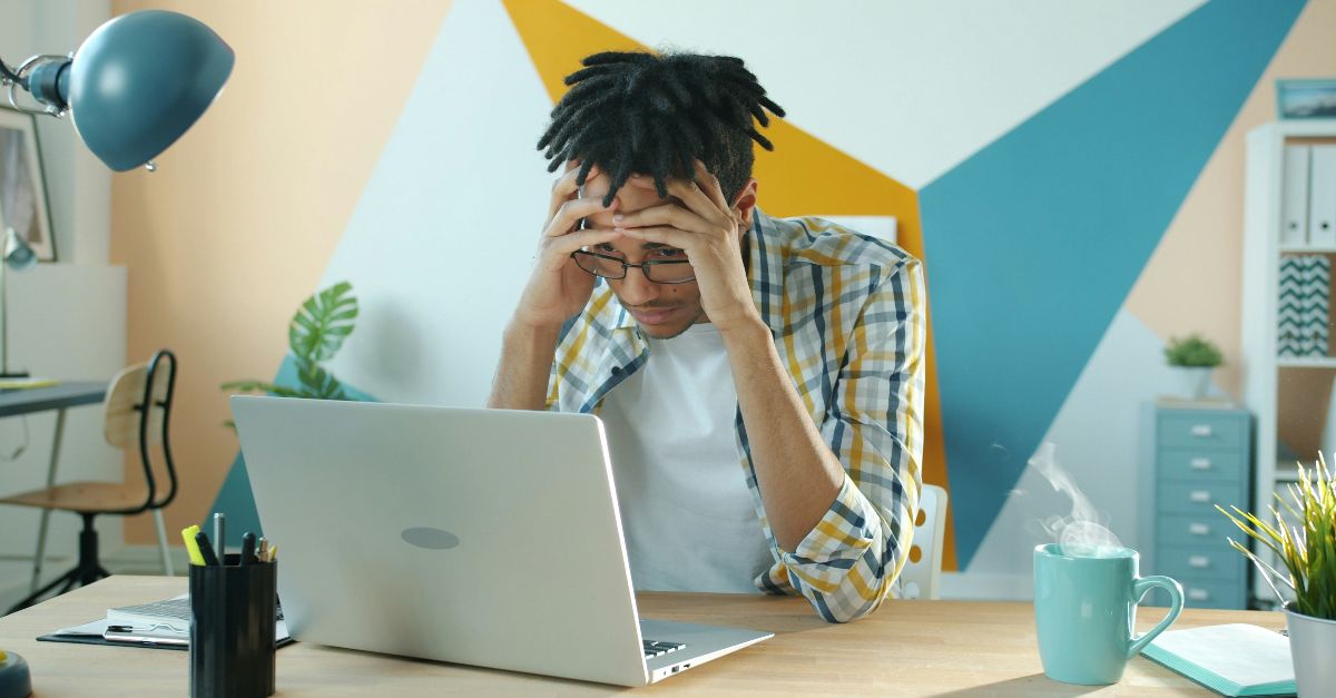 Man holding head in frustration at desk with laptop.