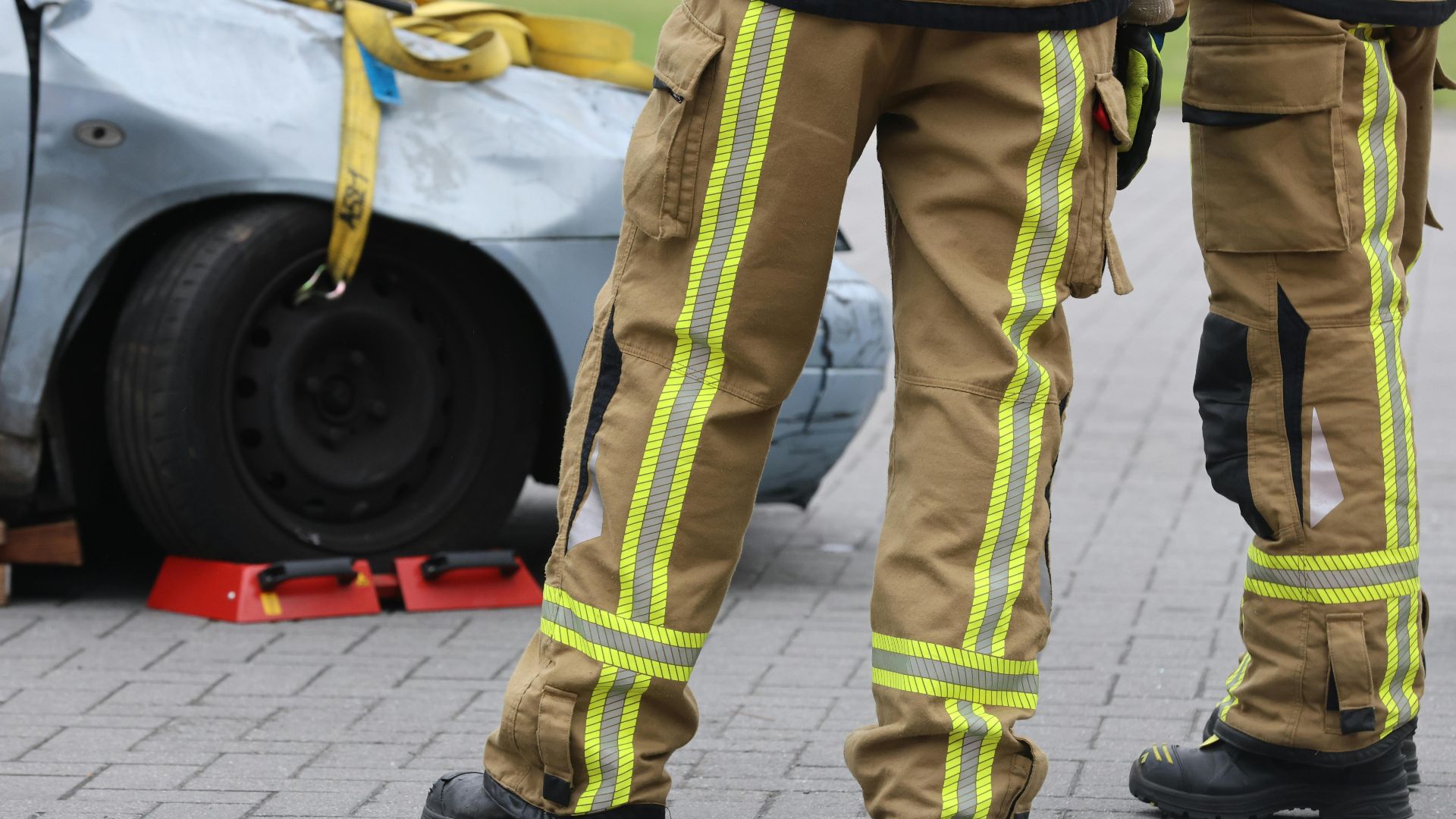 Firefighters inspecting a car accident wearing protective gear. Focus on pants and footwear.