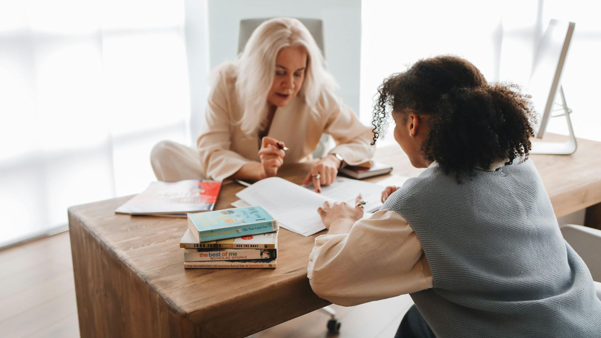 A tutor and student engaged in a learning session with books and notes on a table.