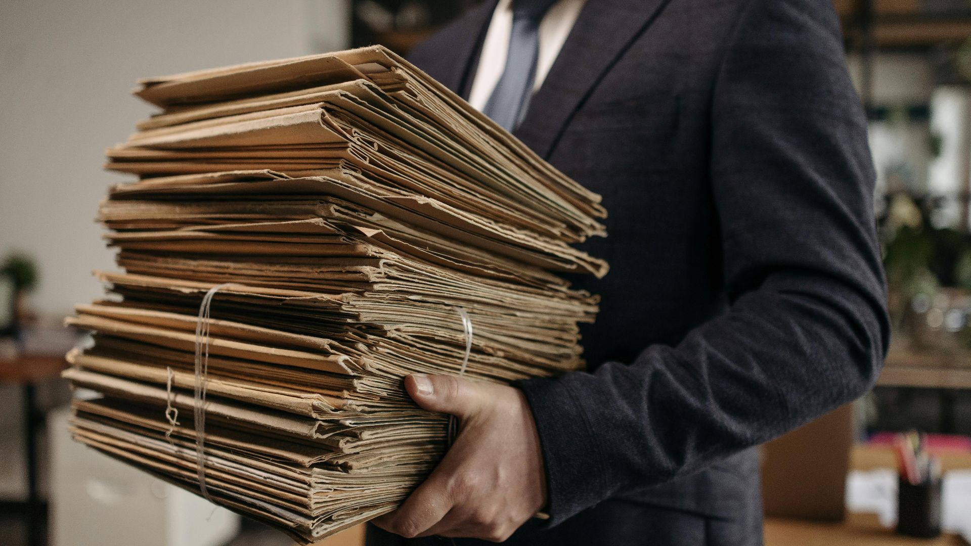 Close-up of business professional holding a large stack of brown folders in an office setting.