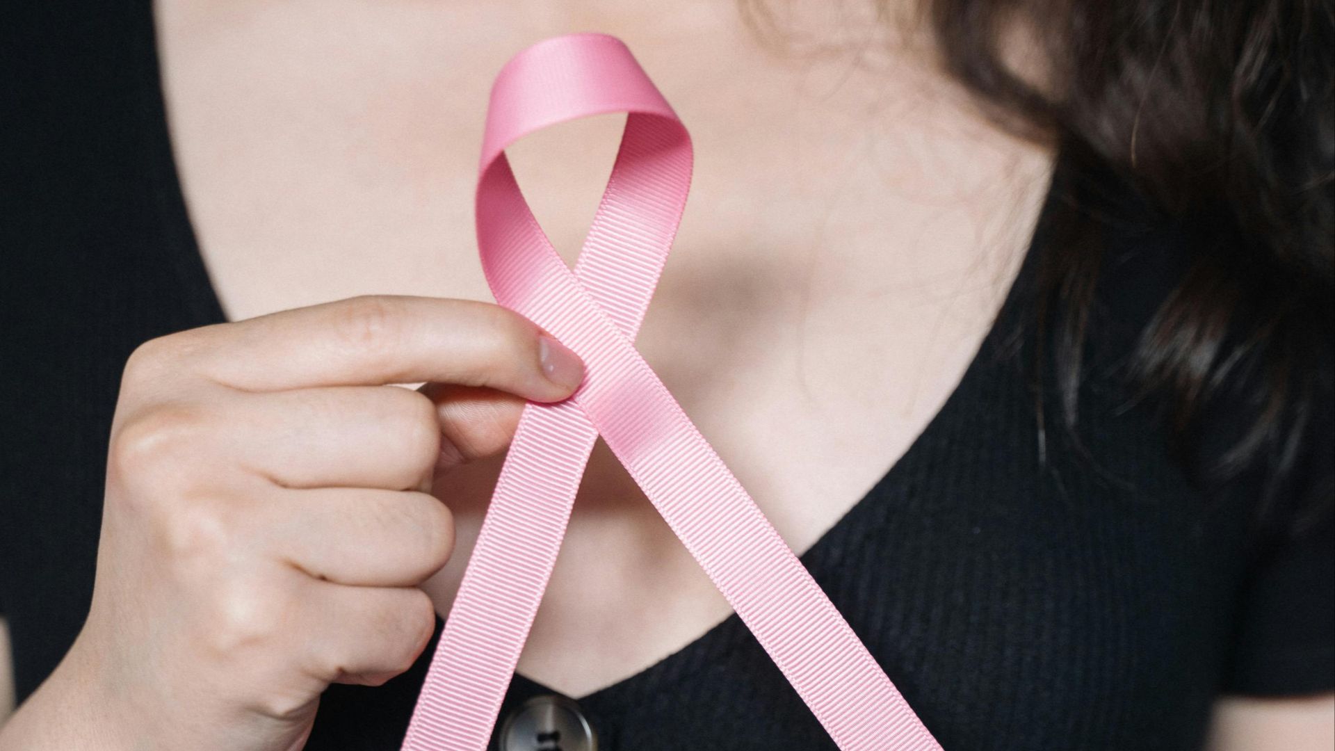 A woman holds a pink ribbon symbolizing breast cancer awareness, promoting health advocacy.