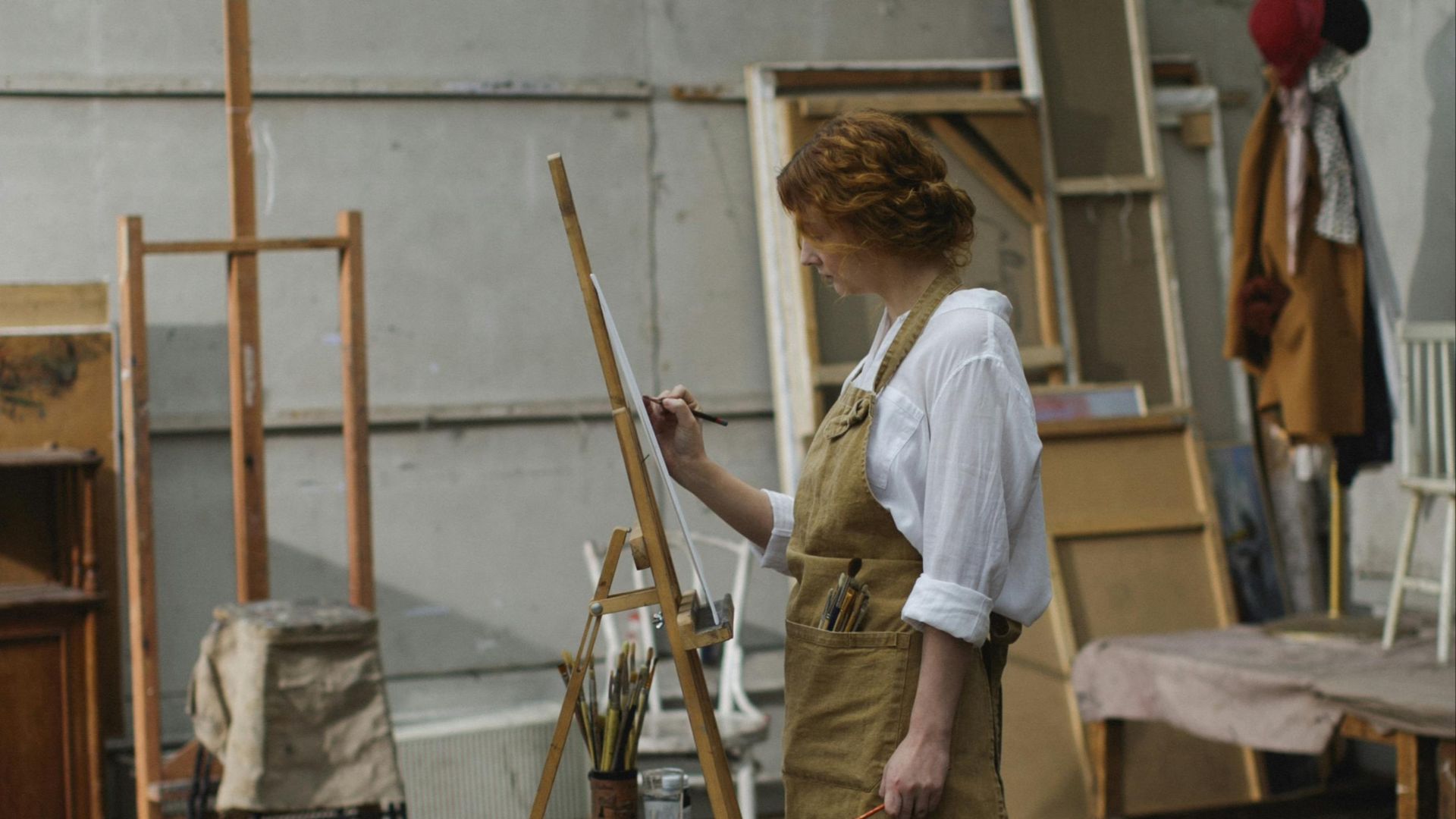 Woman artist in studio painting on canvas, surrounded by art and easels.