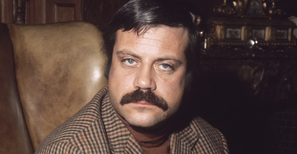 British actor Oliver Reed (1938 - 1999) sitting in an armchair in his huge ex-monastery home