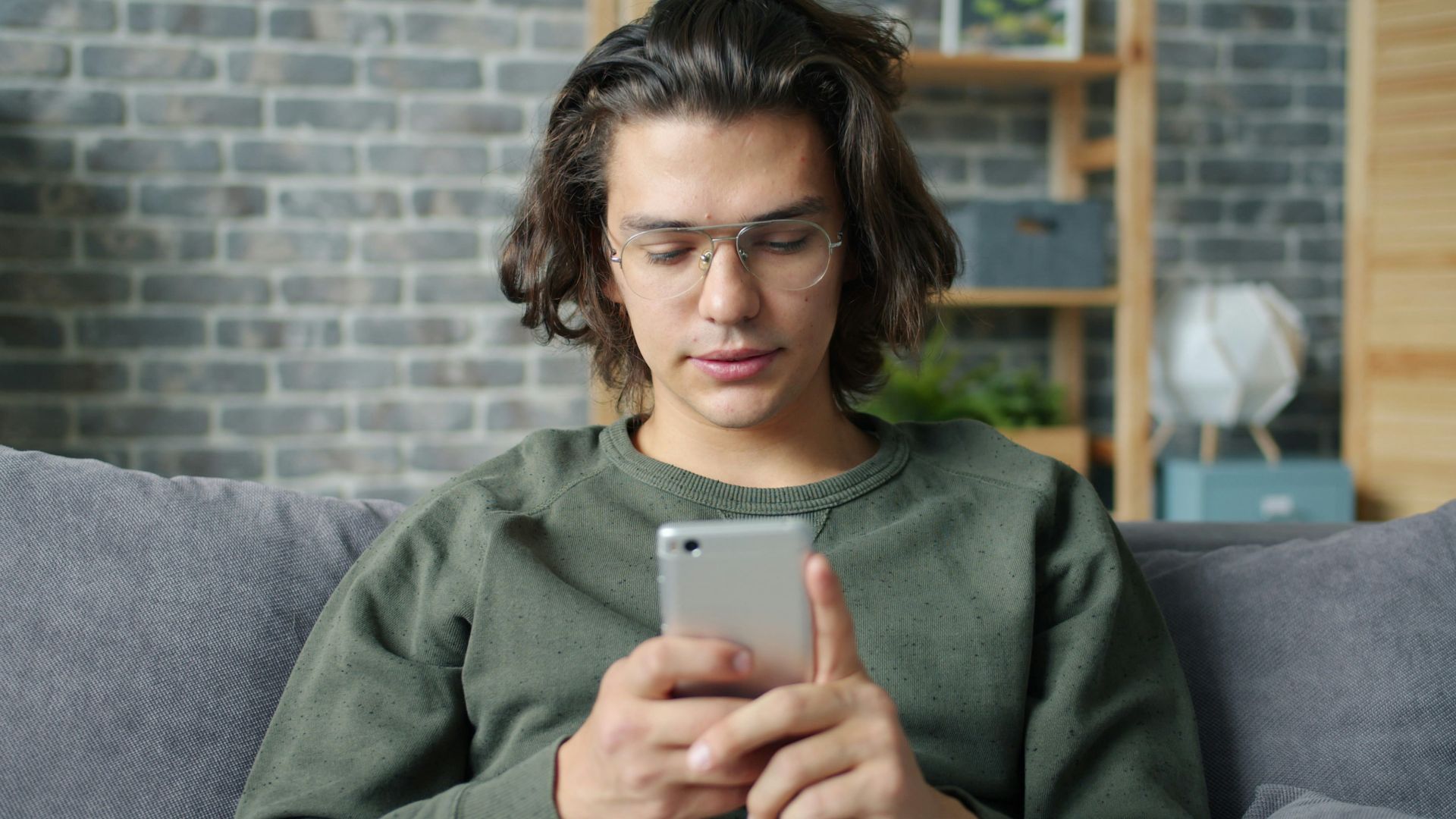 Young man with glasses using a smartphone on couch.