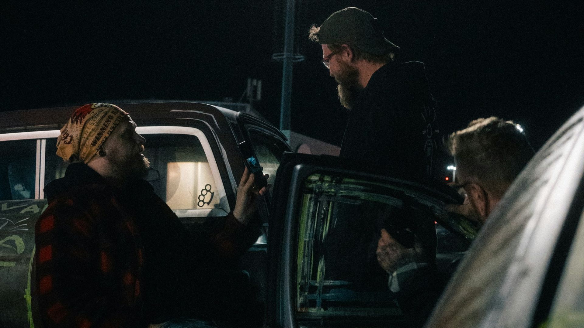 Three men talking near cars at night
