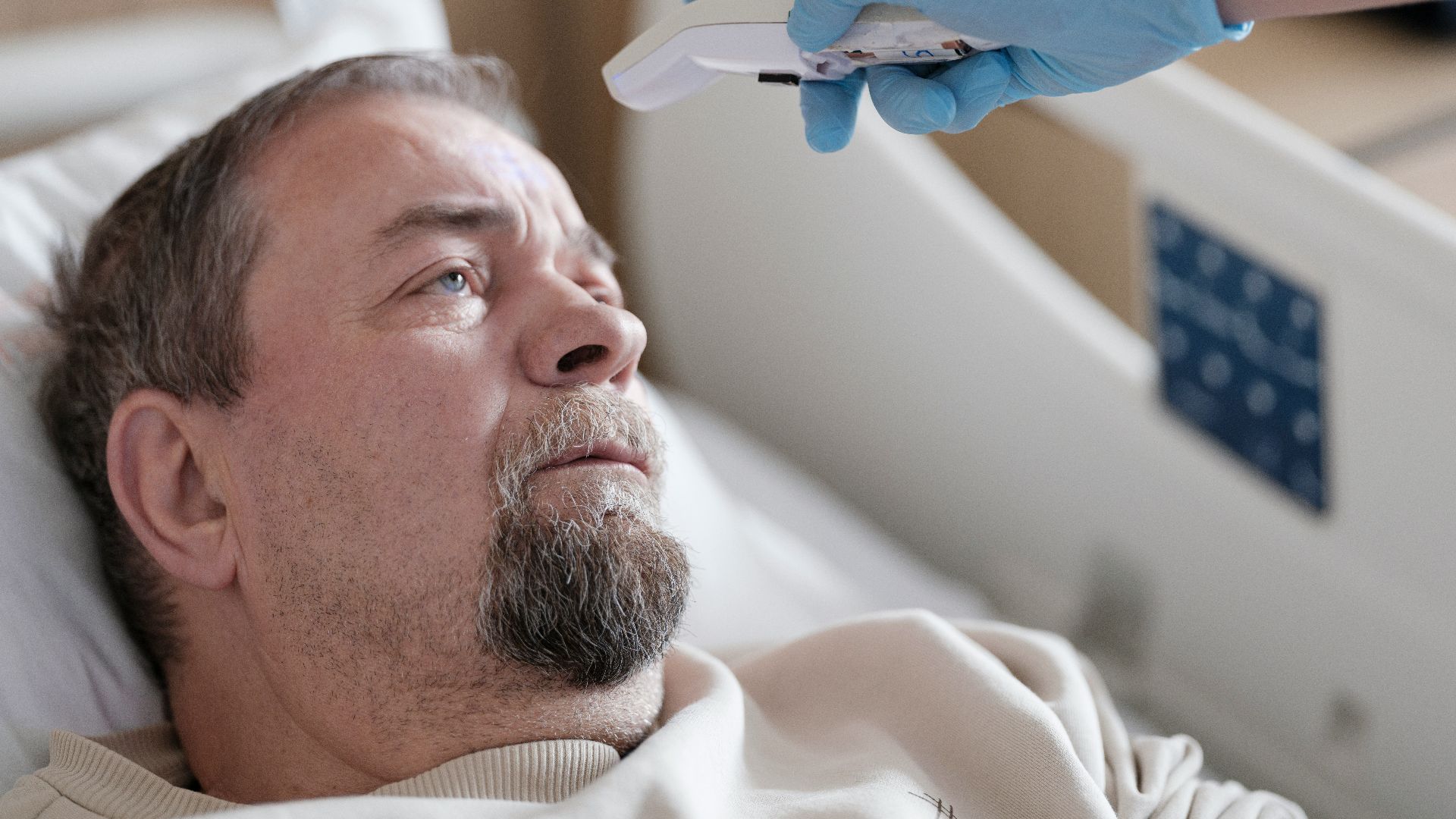 a man laying in a hospital bed with a thermometer in his hand
