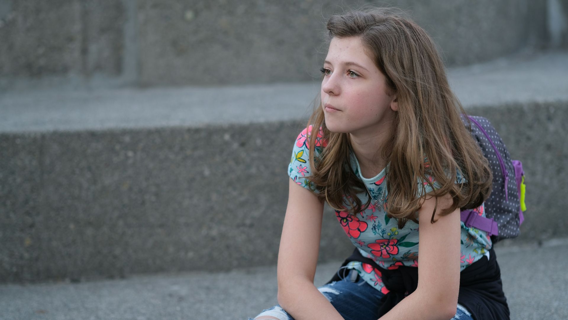 A young girl sitting on steps with a backpack on