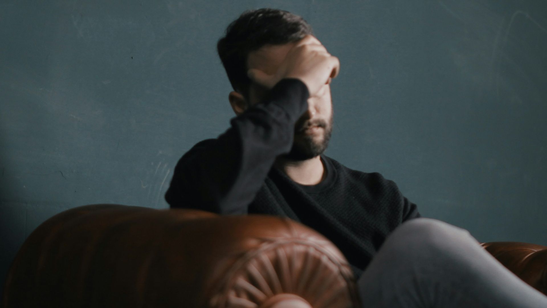a man holds his head while sitting on a sofa