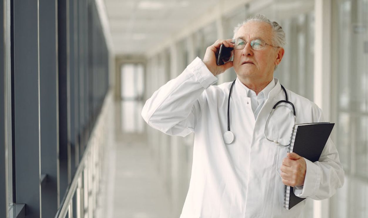 Serious doctor in medical uniform talking on cellphone in clinic