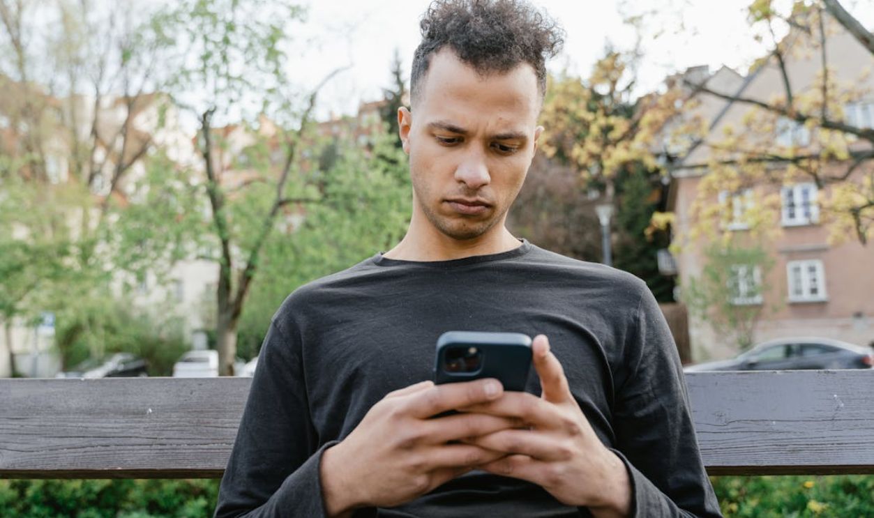 Man Sitting Outdoors Texting on a Smartphone