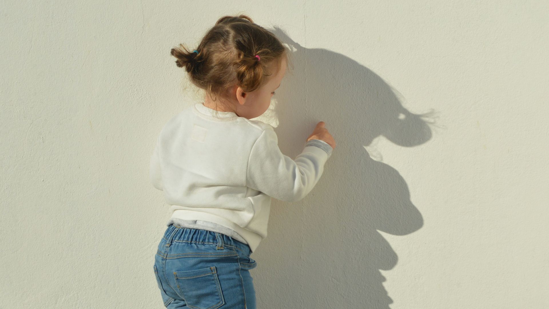 child touching white painted wall during daytime
