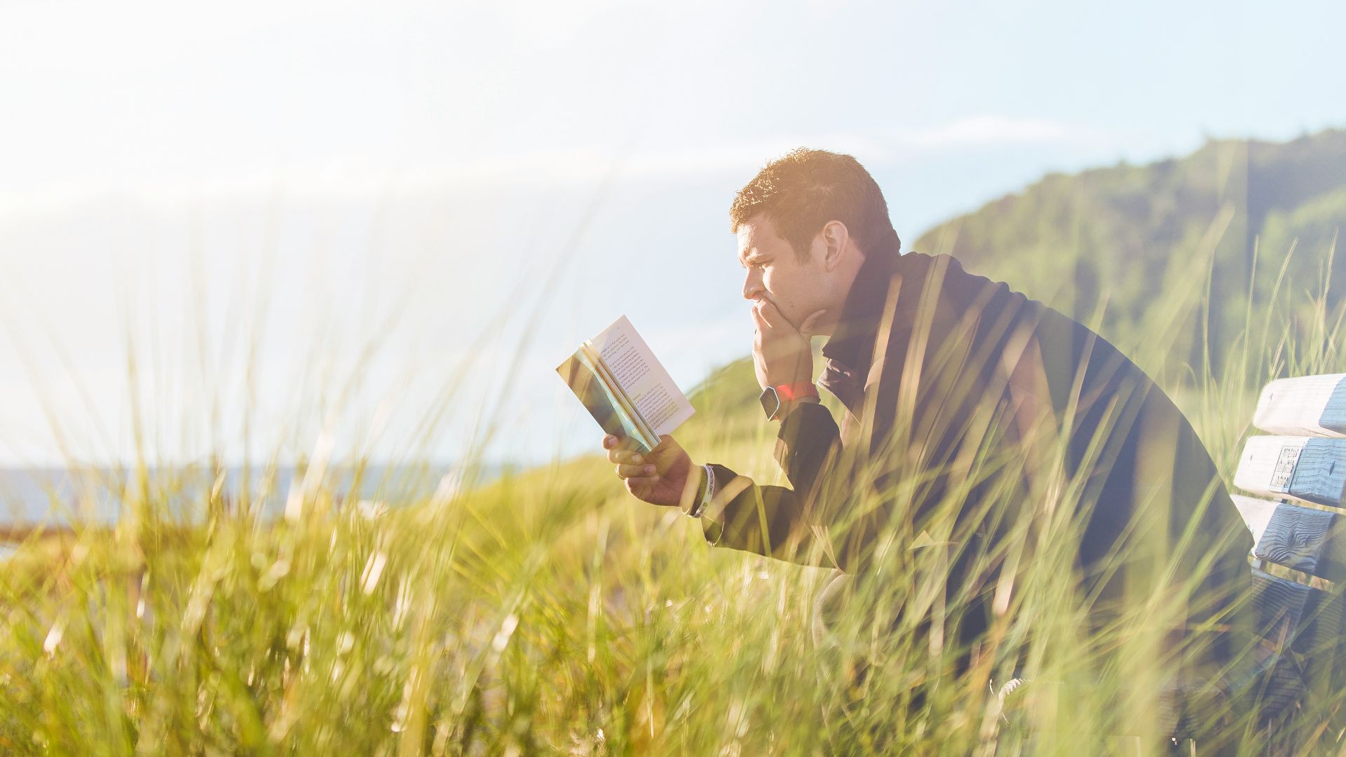 man reading book on beach near lake during daytime
