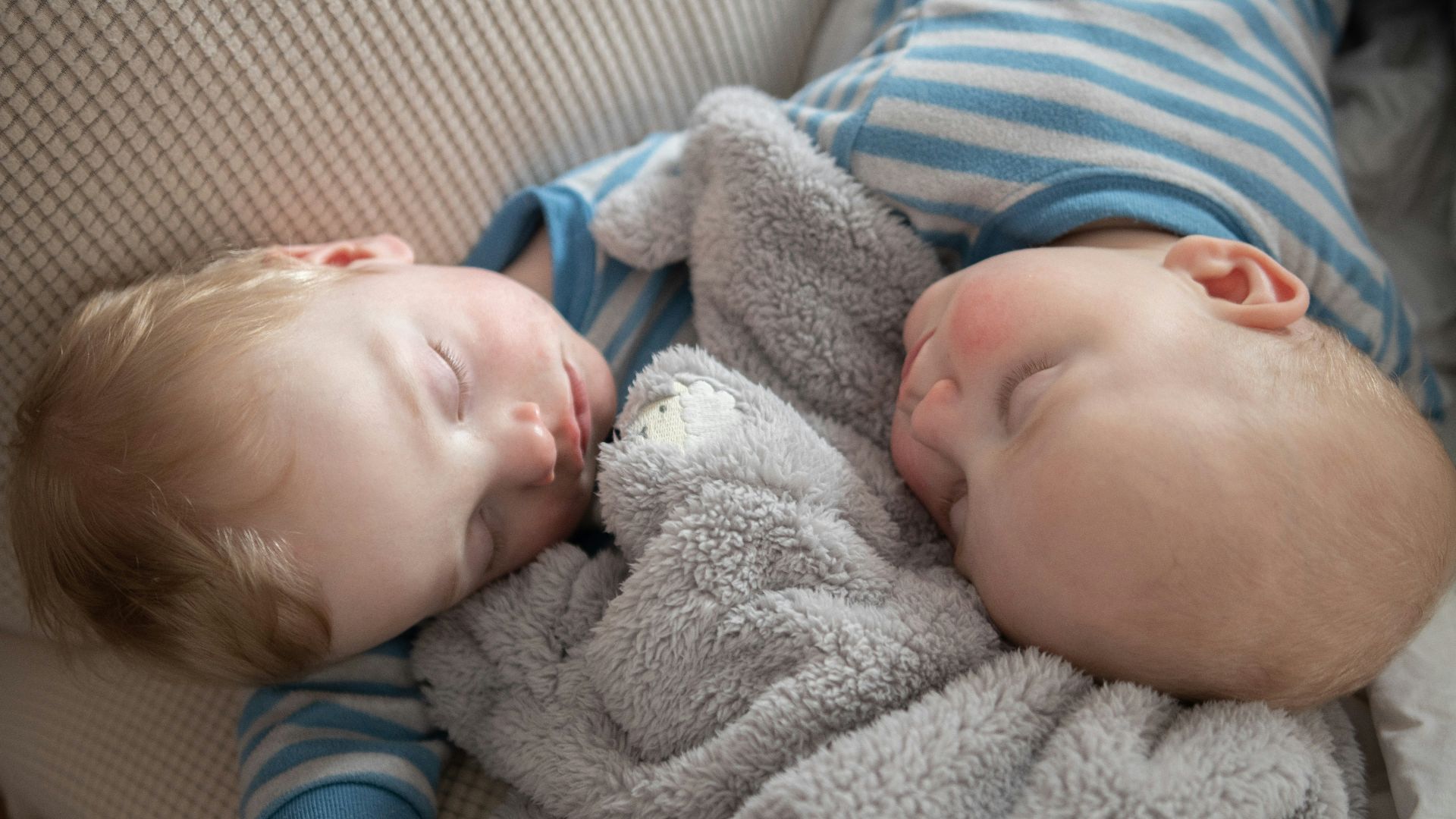 a couple of babies laying next to each other on a couch