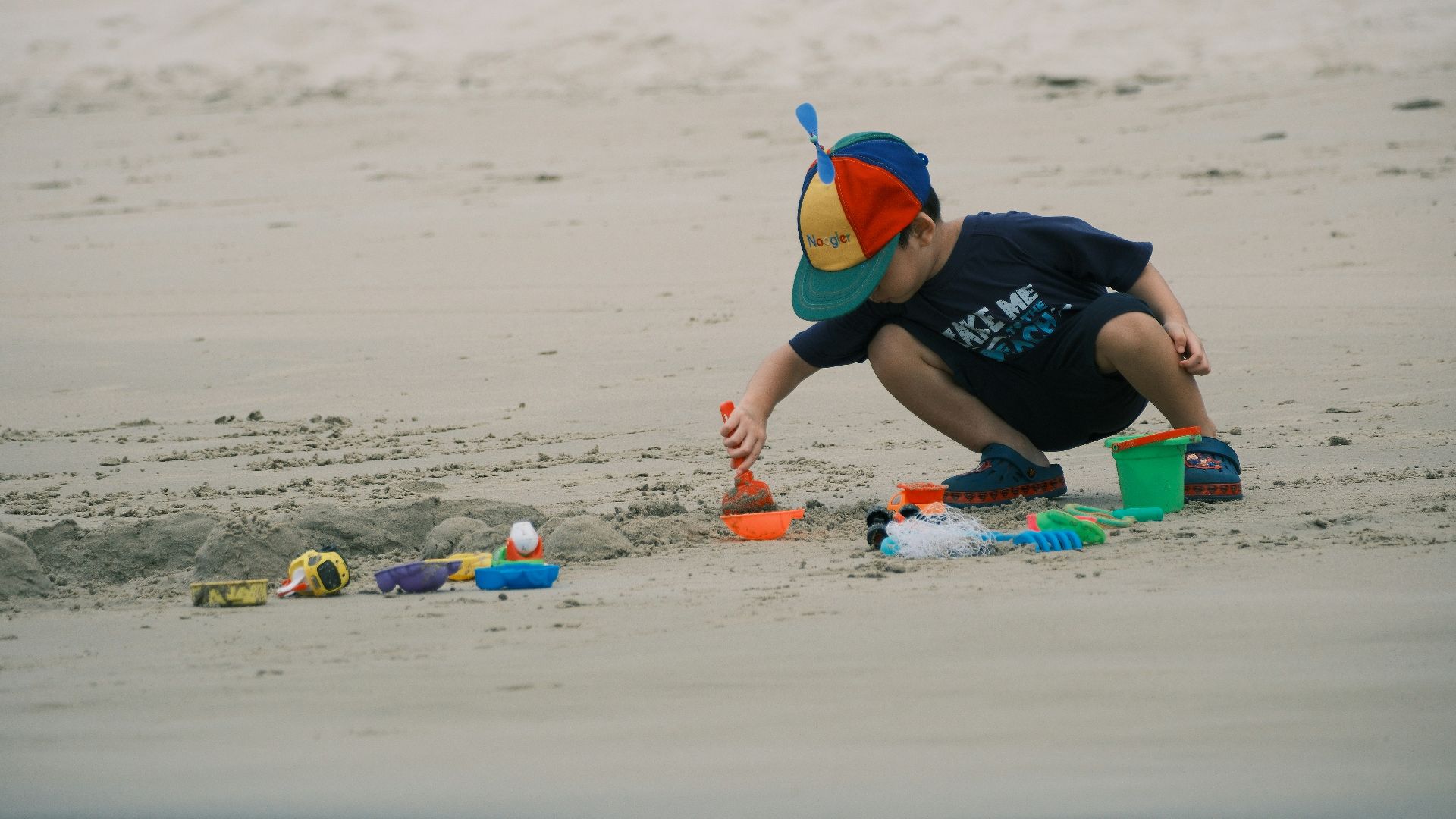A young boy plays with sand toys on the beach.