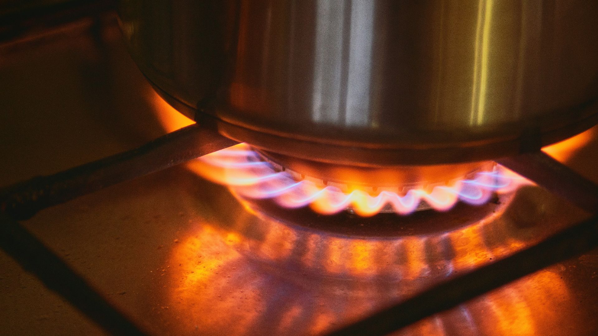 A pot sits on a gas stove burner with flames.